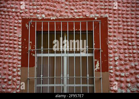 Koloniale Gebäudefassade mit einer roten Steinmauer und einem Fenster mit handgefertigten Eisengittern in Santiago de Querétaro, Mexiko. Stockfoto