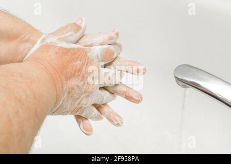 Älterer Mann wäscht die Hände mit Seife unter fließendem Wasser in der Nahaufnahme des Badezimmers, Empfehlung für häufiges Händewaschen, Haushaltshygiene. Stockfoto