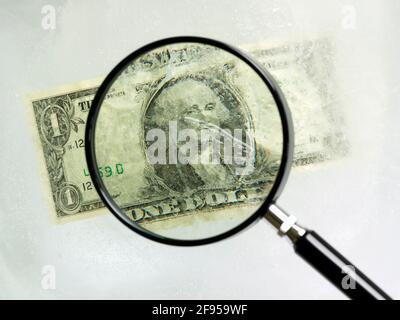 Der amerikanische Dollar-Schein ist in Eis gehüllt und wird durch eine Lupe betrachtet Glas Stockfoto