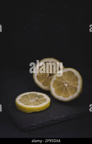 Zitrone in drei Stücke geschnitten, auf einer schwarzen Schieferplatte liegend, vertikal mit Kopierraum Stockfoto