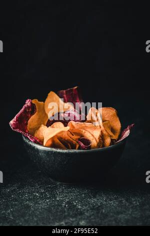 Schwarze Schale auf schwarzem Hintergrund mit einer Variation von Rote Beete, Süßkartoffeln und Pastinak-Chips mit Kopierraum Stockfoto