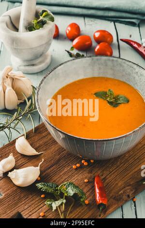 Köstliche, farbige Linsensuppe mit Herbes, Tomaten, Chili und Knoblauch auf einem grauen Tisch. Vertikal. Stockfoto