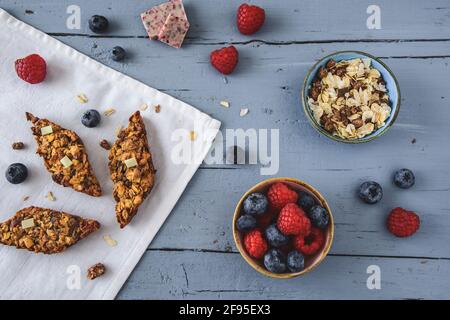 Hausgemachte Beeren-Müsliriegel, dekorieren mit Heidelbeeren und Himbeeren, Beerenschokolade und Getreide, liegen auf einem hellblauen Tisch. Draufsicht. Stockfoto