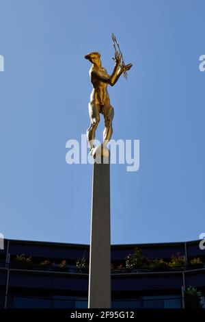 London, Großbritannien - 4. April 2021: Die vergoldete Bronzefigur von Helios, dem allsehenden Sonnengott der griechischen Mythologie, der den zentralen Innenhof des Fernsehzentrums in White City schmückt. Die Statue, die vom Bildhauer T B Huxley-Jones entworfen wurde, wurde für den ehemaligen BBC-Sender, der 1960 eröffnet wurde, in Auftrag gegeben. Die Statue stellt die Ausstrahlung des Fernsehlichts auf der ganzen Welt dar und sitzt in der Mitte eines Brunnens und zwei liegende Figuren, die Ton und Vision repräsentieren, die beiden Komponenten des Fernsehens. Stockfoto