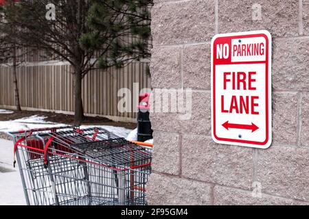 Ein „No Parking“, rotes vertikales Schild der Fire Lane mit doppelköpfigen Pfeilen, die an einer beigefarbenen Ziegelmauer vor einem Supermarkt in London, Ontario, Kanada, befestigt sind. Stockfoto