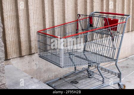 Ein silberner und roter Metallwagen, der an einem trüben und bewölkten Tag im Winter vor einem Supermarkt in London, Ontario, Kanada, an einer beigen Wand geparkt ist. Stockfoto