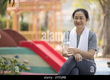 Eine ältere sportliche Frau trinkt Wasser aus einer Flasche, nachdem sie im Park gelaufen ist. Stockfoto