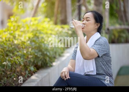 Eine ältere sportliche Frau trinkt Wasser aus einer Flasche, nachdem sie im Park gelaufen ist. Stockfoto