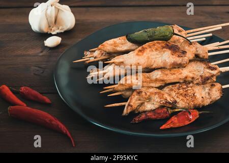 Teller mit gegrillten Hähnchenspießen, Knoblauch und rotem Chili auf dunklem Holz. Stockfoto
