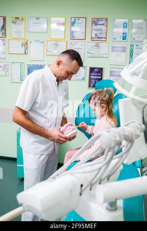 Professioneller Arzt, pädiatrischer Zahnarzt lehrt ein Kind, seine Zähne zu putzen. Zahnarztpraxis für Patientenuntersuchung. Der Prozess der zahnärztlichen Behandlung in einem Stockfoto