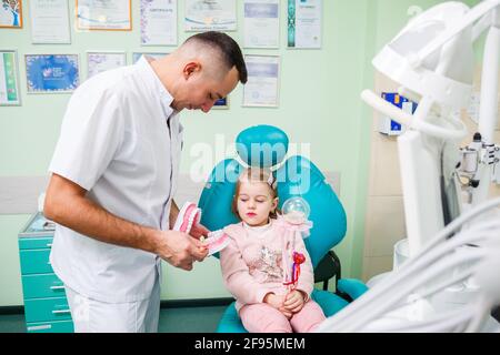 Professioneller Arzt, pädiatrischer Zahnarzt lehrt ein Kind, seine Zähne zu putzen. Zahnarztpraxis für Patientenuntersuchung. Der Prozess der zahnärztlichen Behandlung in einem Stockfoto