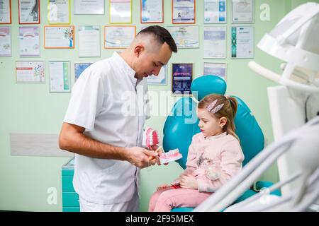 Professioneller Arzt, pädiatrischer Zahnarzt lehrt ein Kind, seine Zähne zu putzen. Zahnarztpraxis für Patientenuntersuchung. Der Prozess der zahnärztlichen Behandlung in einem Stockfoto