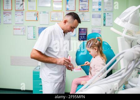 Professioneller Arzt, pädiatrischer Zahnarzt lehrt ein Kind, seine Zähne zu putzen. Zahnarztpraxis für Patientenuntersuchung. Der Prozess der zahnärztlichen Behandlung in einem Stockfoto