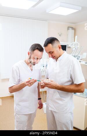 Zahnärzte Ärzte stehen im Büro, Klinik mit Stuhl, Werkzeuge. Zahnarztarbeitsplatz. Kieferorthopäden halten sich in den Händen und untersuchen den Kieferabguss Stockfoto