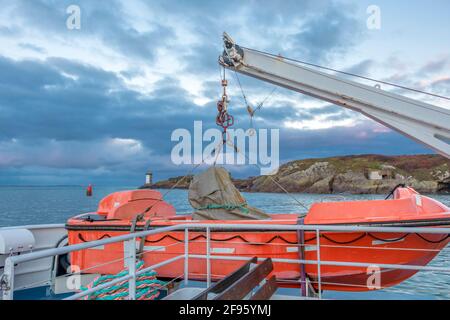 Transport und Sicherheit auf See. Rettungsinsel auf dem Fährdeck, orangefarbenes Rettungsboot bereit für die Evakuierung vom Bord, über einem blauen Meer an der Seite von hängend Stockfoto