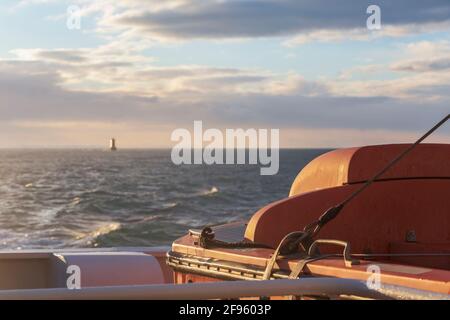 Transport und Sicherheit auf See. Rettungsinsel auf dem Fährdeck, orangefarbenes Rettungsboot bereit für die Evakuierung vom Bord, über einem blauen Meer an der Seite von hängend Stockfoto