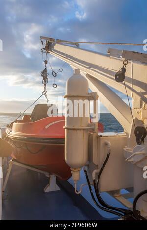 Transport und Sicherheit auf See. Rettungsinsel auf dem Fährdeck, orangefarbenes Rettungsboot bereit für die Evakuierung vom Bord, über einem blauen Meer an der Seite von hängend Stockfoto