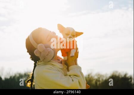 Porträt eines glücklichen Teenagers mit ihrem kleinen chihuahua-Hund. Ein Mädchen auf dem Hintergrund der Natur umarmt ihren Chihuahua Hund in Kleidung. Stockfoto