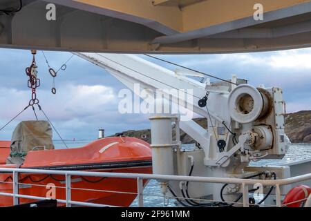 Transport und Sicherheit auf See. Rettungsinsel auf dem Fährdeck, orangefarbenes Rettungsboot bereit für die Evakuierung vom Bord, über einem blauen Meer an der Seite von hängend Stockfoto