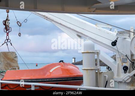 Transport und Sicherheit auf See. Rettungsinsel auf dem Fährdeck, orangefarbenes Rettungsboot bereit für die Evakuierung vom Bord, über einem blauen Meer an der Seite von hängend Stockfoto