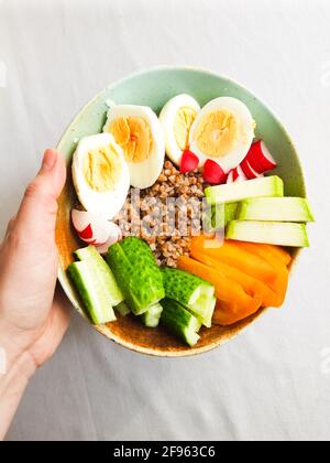 Frauenhand mit einer Schüssel mit gekochten Eiern, Gemüse und Buckweata Stockfoto