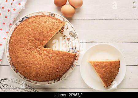 Hausgemachter Biskuitkuchen in Scheiben geschnitten und Eier auf einem Weißer Holztisch Stockfoto