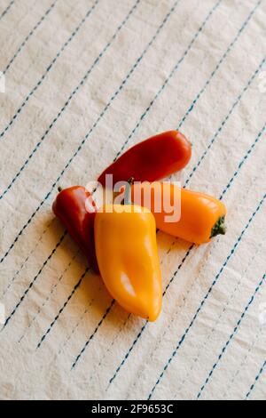 Nahaufnahme von rohen Bio-Mini-Cocktail roten, orangen und gelben Paprika auf rustikaler weißer Tischdecke Stockfoto