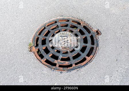 Samara, Russland - 17. August 2020: Rostige Metallschachtabdeckung auf städtischer Straßenbelag. Rundes Kanalloch für die Abflussrinnerkanäle Stockfoto