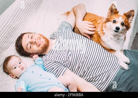 Vater und Baby liegen mit dem Hund auf dem Bett. Nahaufnahme im Hochformat Stockfoto