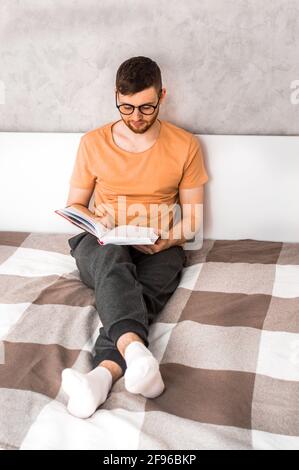 Junger Mann liest ein Buch im Bett. Vertikales Foto Stockfoto