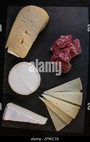Vertikale Aufnahme von verschiedenen Käsesorten und Salami auf Eine schwarze Oberfläche Stockfoto