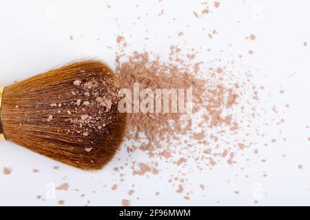 Verstreute, bräunliche Puder- und Make-up-Bürste für das Gesicht auf weißem Hintergrund. Speicherplatz kopieren. Flach liegend. Stockfoto