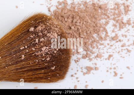 Verstreute, bräunliche Puder- und Make-up-Bürste für das Gesicht auf weißem Hintergrund. Speicherplatz kopieren. Flach liegend. Stockfoto