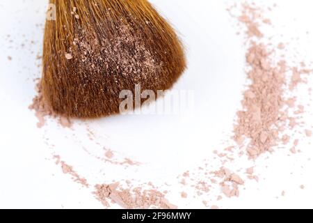 Verstreute, bräunliche Puder- und Make-up-Bürste für das Gesicht auf weißem Hintergrund. Speicherplatz kopieren. Flach liegend. Stockfoto