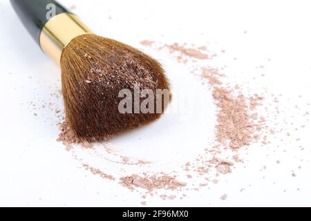 Verstreute, bräunliche Puder- und Make-up-Bürste für das Gesicht auf weißem Hintergrund. Speicherplatz kopieren. Stockfoto