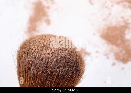 Verstreute, bräunliche Puder- und Make-up-Bürste für das Gesicht auf weißem Hintergrund. Stockfoto