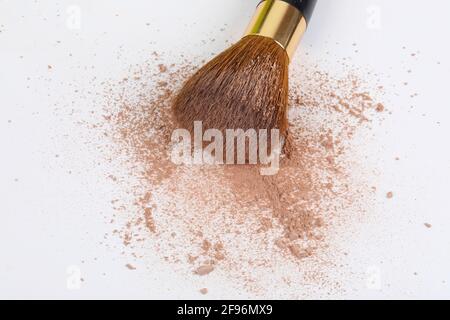 Verstreute, bräunliche Puder- und Make-up-Bürste für das Gesicht auf weißem Hintergrund. Speicherplatz kopieren. Stockfoto