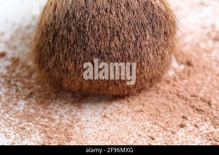 Verstreute, bräunliche Puder- und Make-up-Bürste für das Gesicht auf weißem Hintergrund. Nahaufnahme. Vorderansicht. Stockfoto