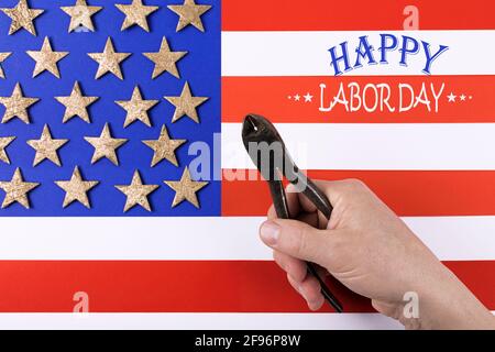 Alte Metallzange in der Hand des Mannes über der amerikanischen Flagge. Inschrift Happy Labor Day. Internationale Feier. Flach liegend. Stockfoto