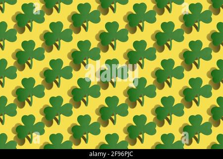 St. Patrick's Day Hintergrund. Kreatives nahtloses Musterlayout mit grünen Kleeblättern und harten Schatten auf gelbem Hintergrund. Stockfoto