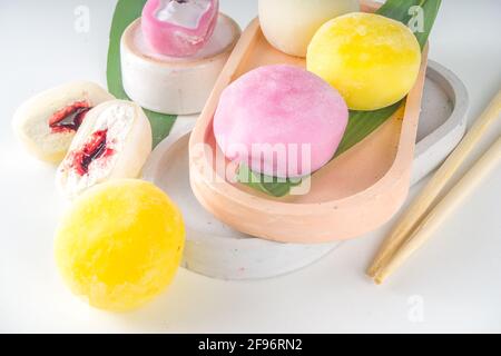 Traditionelles japanisches Dessert-Mochi. Buntes Mochi-Eis auf einem weißen Tisch, ganz und mit Beerenfrüchten, Fruchtfüllung geschnitten Stockfoto
