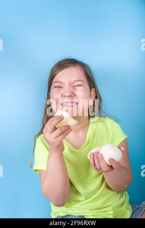 Niedliche Vorschulkinder genießen japanische süße Mochi. Mädchen Kind essen trendige Mochi Eis mit Fruchtaromen, auf einem hellblauen Hintergrund Stockfoto
