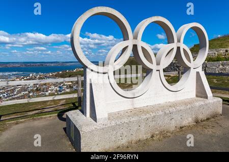 Olympic-Ringe-Skulptur mit der Chaesil Bank und der Fleet Lagoon in der Ferne in Portland, Weymouth, Dorset, Großbritannien im April Stockfoto