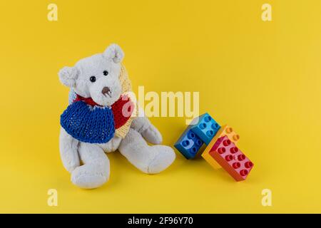 Hintergrund des Autismus-Bewusstseins. Teddybär mit gestricktem Schal in Puzzlemuster-Farben auf gelbem Hintergrund. Speicherplatz kopieren. Stockfoto