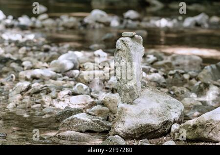 Gestapelte Felsen, balanciert in einem Streambed. Balancierter Felsstapel an einem Bach, mit einem kleinen roten Marienkäfer auf der Oberseite, umgeben von einem Bach. Stockfoto