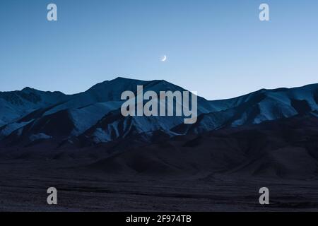 Der Mond steigt am Abend über den schneebedeckten Bergen auf Nachdem die Sonne untergegangen ist Stockfoto