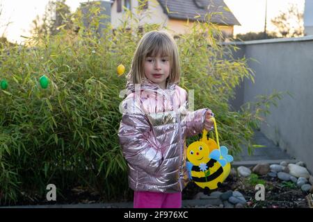 Kleines Mädchen auf der Suche nach Ostereiern im Garten mit ihrem bienenförmigen Korb. Stockfoto