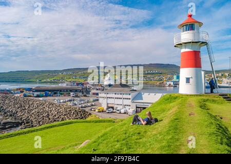 Ein einheimisches Mädchen liest ein Buch an einem alten Leuchtturm und einer Festung im Hafen von Torshavn, der Hauptstadt des Färöer-Archipels im Atlantischen Ozean, Sum Stockfoto