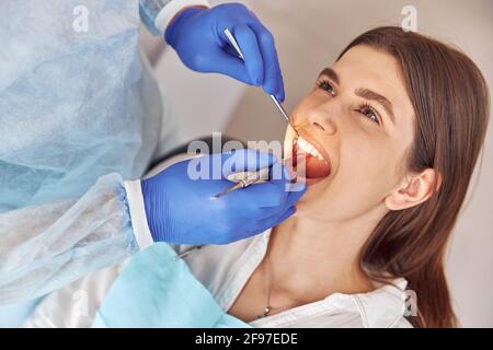 Porträt eines jungen Zahnarztes in Handschuhen, die Zähne von Frauen untersuchen Kunde im Krankenhaus Stockfoto