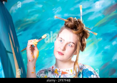 Junge Frau mit Updo und Pinsel in den Haaren beim Malen. Stockfoto